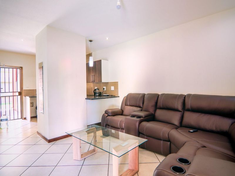Open plan living area featuring tiled flooring and a compact kitchen corner with built-in cabinetry, leading to an exterior entrance.