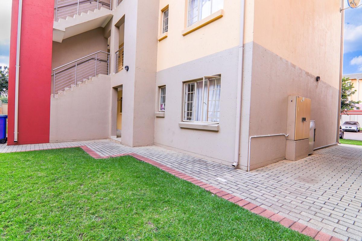 Exterior view of the apartment building featuring a paved walkway, small lawn area, and external staircase access.