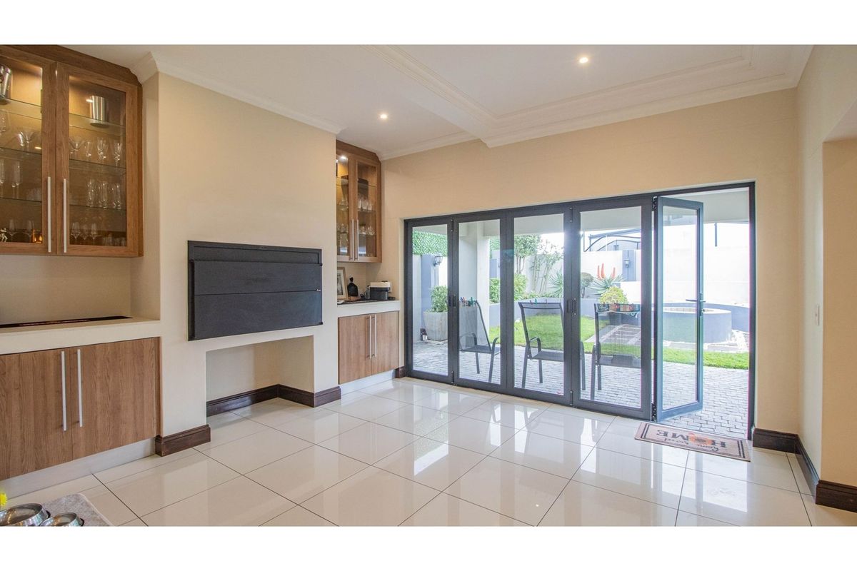 Living area featuring built-in wooden cabinetry, a wall-mounted fireplace, and large folding glass doors opening onto a paved patio and garden.