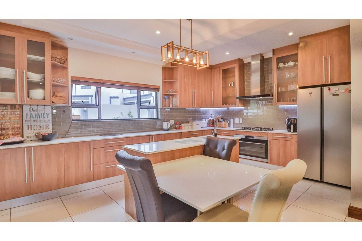 Modern kitchen featuring light wood cabinetry, stone countertops, subway tile backsplash, integrated oven, gas hob, and a central island with breakfast seating.
