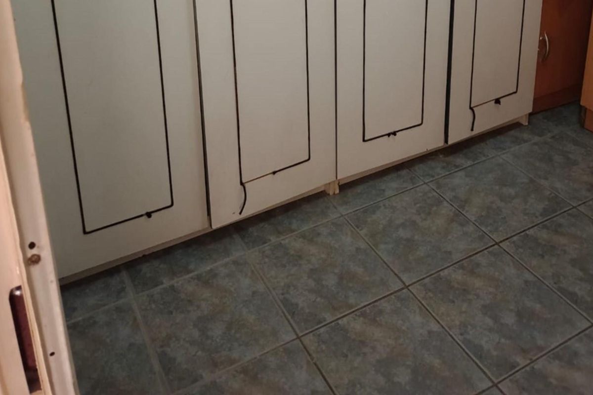 A close-up view of kitchen cabinetry featuring white doors with black trim and dark tiled flooring, showing signs of wear and tear.