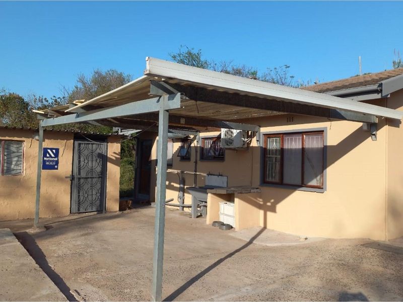 Rear exterior view featuring a covered patio area, external wash basin, security gates, and air conditioning unit mounted on the wall.