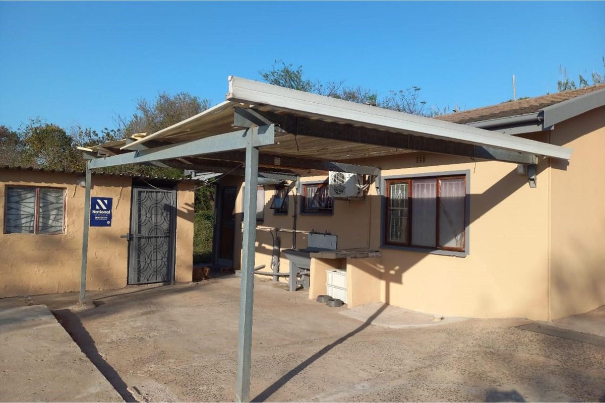 Rear exterior view featuring a covered patio area, external wash basin, security gates, and air conditioning unit mounted on the wall.