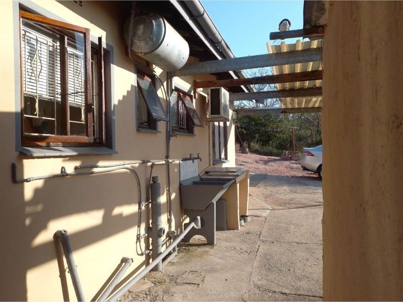 Rear exterior view showing a utility area with an external laundry sink, mounted electric geyser, and air conditioning unit.