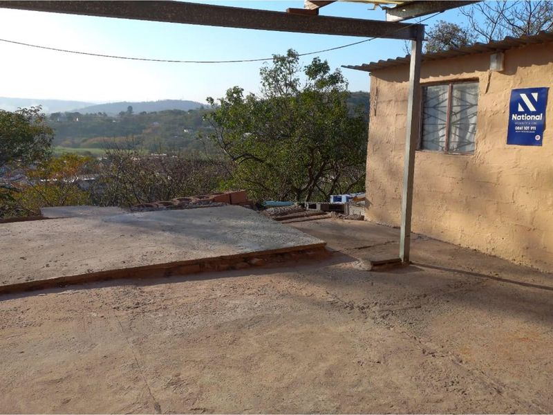 An outdoor patio area featuring a concrete slab, metal support structure, and scenic hillside views, requiring finishing and maintenance.