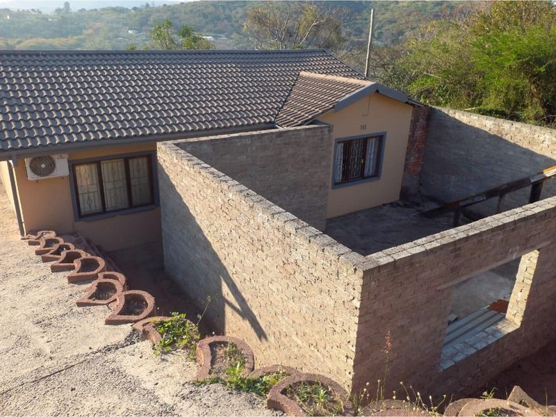 Rear view of the property showing an existing house with an attached unfinished brick construction project and concrete retaining wall features.
