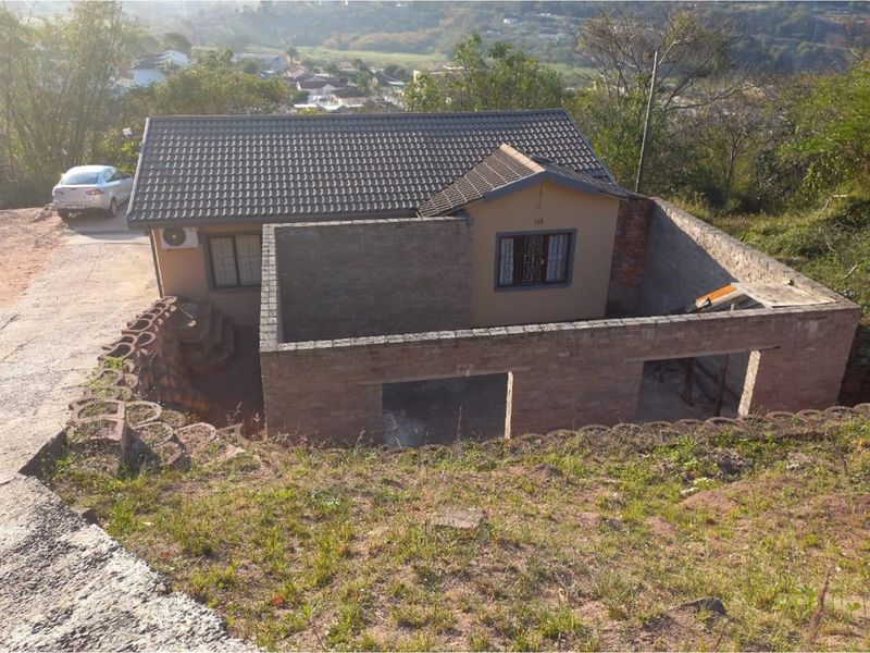 Rear view of a residential property featuring an existing house structure with an ongoing, unfinished brick masonry extension.