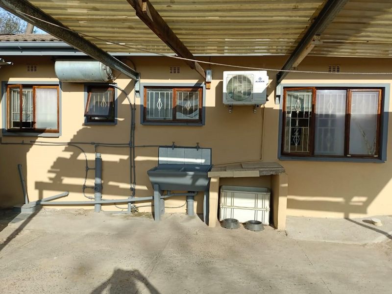 Covered outdoor utility area featuring a concrete sink, external air conditioning unit, and security-fitted windows, providing a functional space for laundry or outdoor tasks.