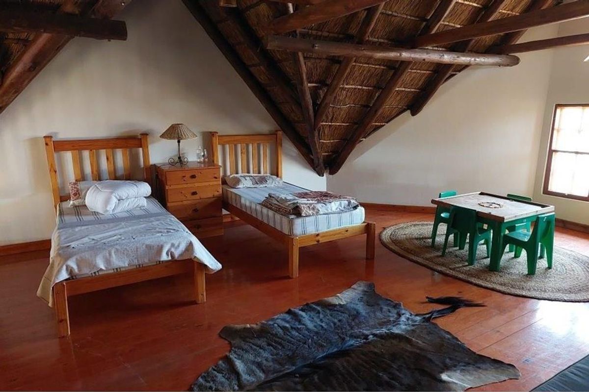 Spacious bedroom featuring a traditional thatched roof with exposed timber beams and warm wooden flooring.