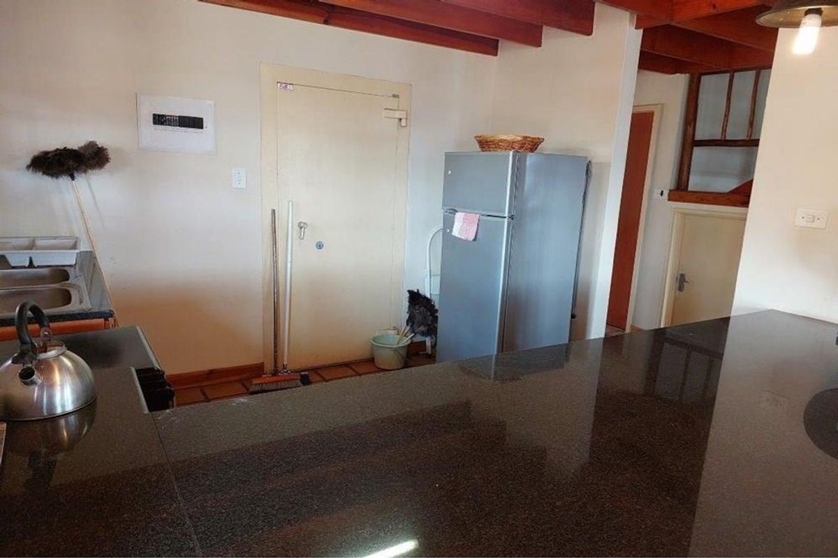 A functional kitchen area featuring a dark granite countertop, exposed timber ceiling beams, and tiled flooring, providing a practical workspace.
