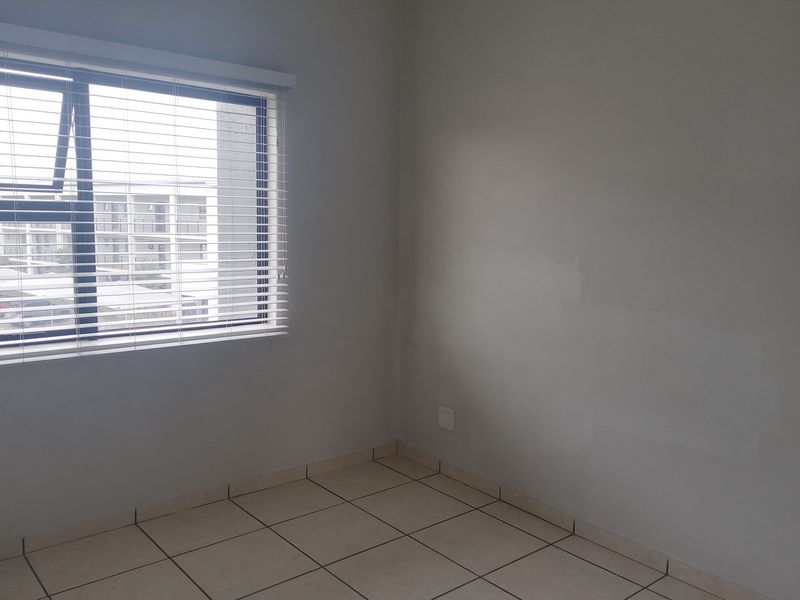 A bright, empty bedroom featuring neutral tiled flooring and a large window with fitted blinds, offering a clean canvas for personalization.