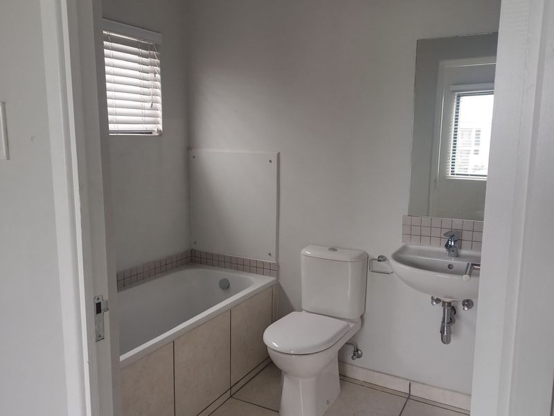 A functional bathroom featuring a built-in bathtub, wall-mounted basin, and toilet, finished with neutral floor tiles and a wall-mounted mirror.