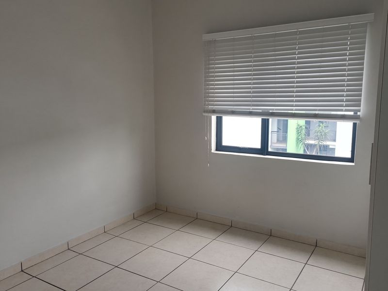 A bright, empty bedroom featuring neutral tiled flooring, white walls, and a window fitted with white venetian blinds.