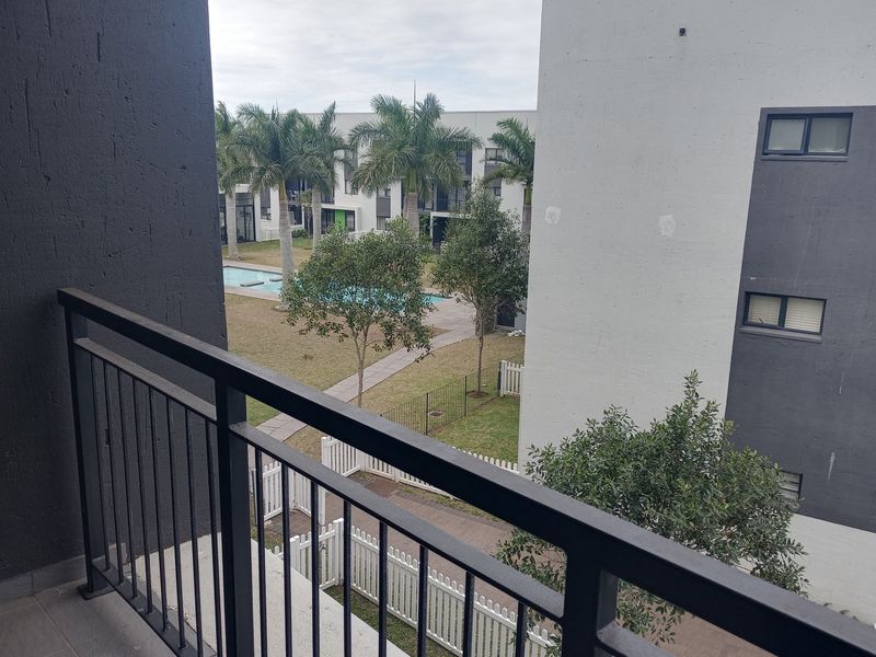 View from a balcony overlooking a communal garden area with a swimming pool and surrounding apartment complex buildings.