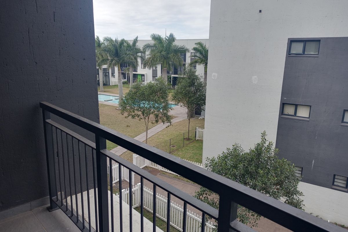 View from a balcony overlooking a communal garden area with a swimming pool and surrounding apartment complex buildings.
