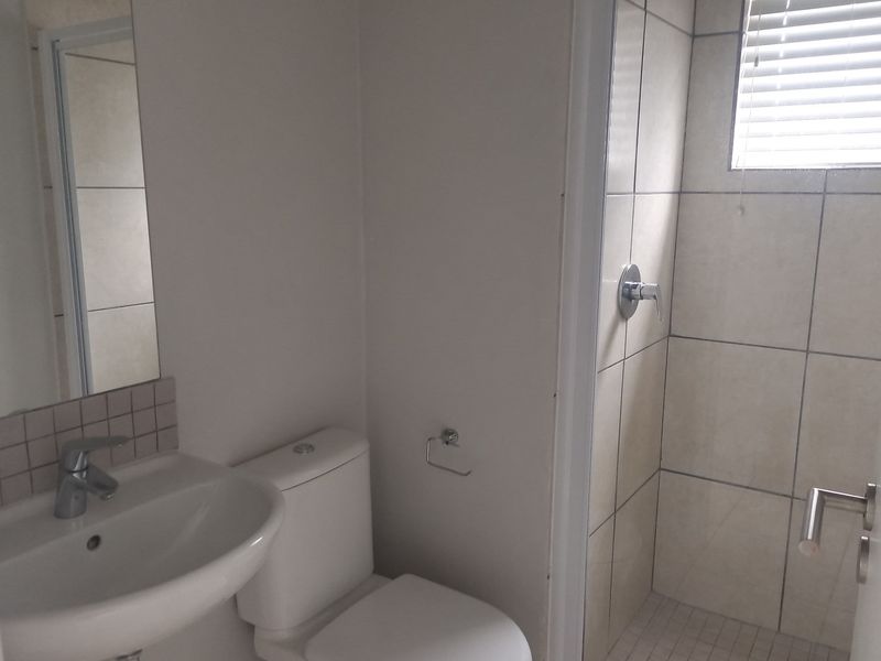A functional bathroom featuring a pedestal basin, toilet, and a tiled shower enclosure with a window.