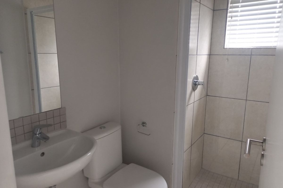 A functional bathroom featuring a pedestal basin, toilet, and a tiled shower enclosure with a window.
