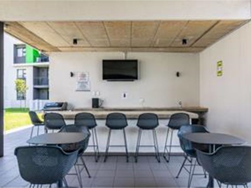 A covered outdoor patio area featuring a built-in bar counter, tiled flooring, and a concrete ceiling, ideal for communal outdoor entertainment.