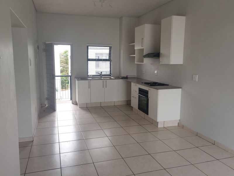 An open-plan kitchen featuring white cabinetry, a built-in oven, hob, and extractor fan, with tiled flooring and direct access to a balcony.