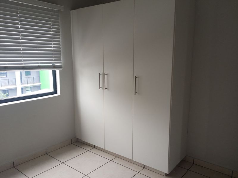 A bedroom featuring built-in white cabinetry and tiled flooring, complemented by a window with fitted blinds.
