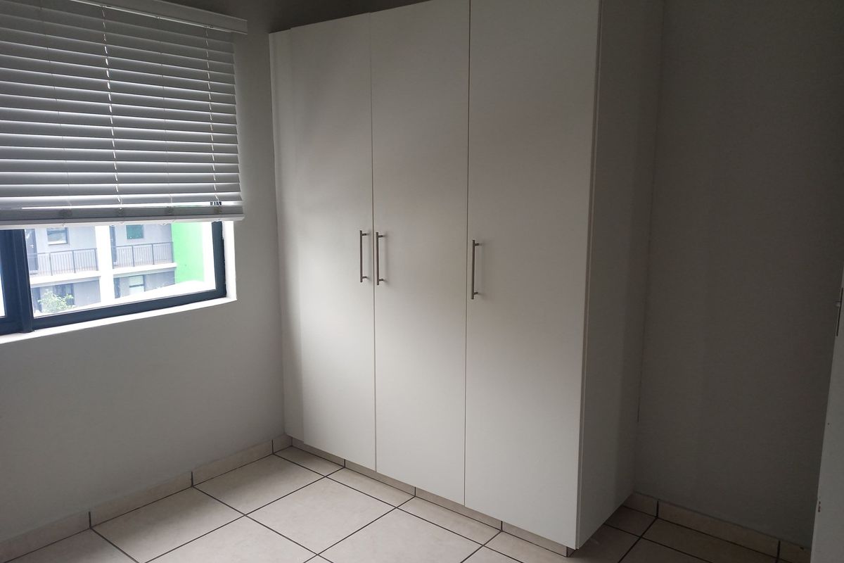 A bedroom featuring built-in white cabinetry and tiled flooring, complemented by a window with fitted blinds.