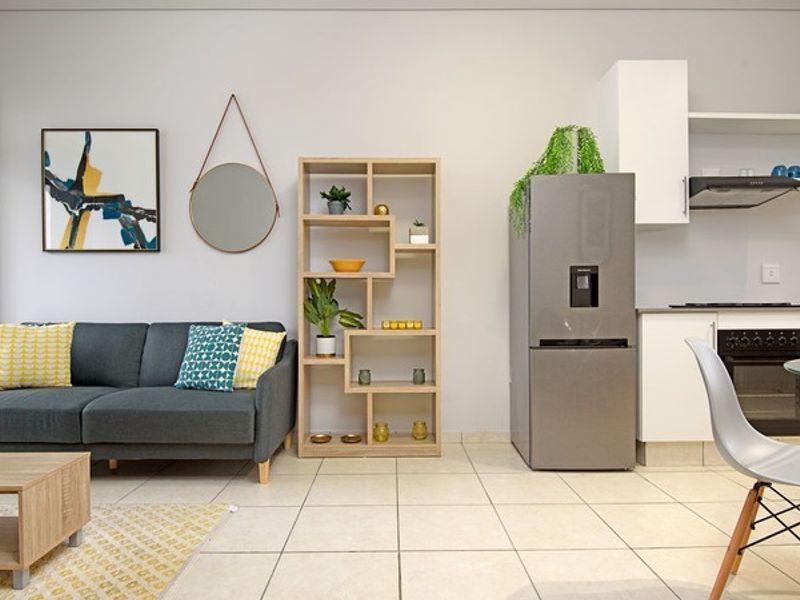 An open-plan living and kitchen area featuring modern white cabinetry, built-in appliances, and neutral tiled flooring throughout.