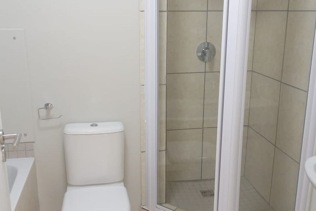 A functional bathroom featuring a shower enclosure, toilet, and washbasin with neutral wall tiling.