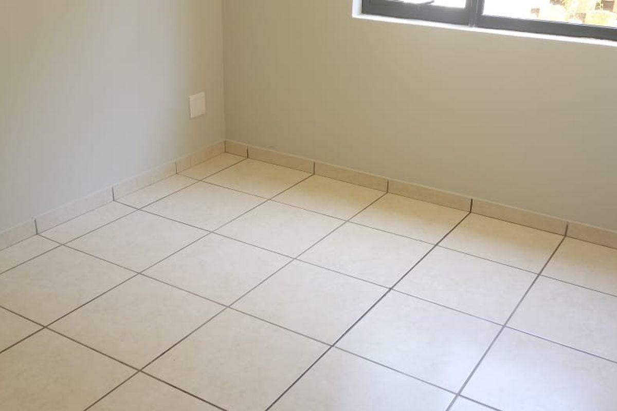 A clean, empty bedroom featuring neutral tiled flooring, a built-in cupboard, and a modern aluminium window frame.