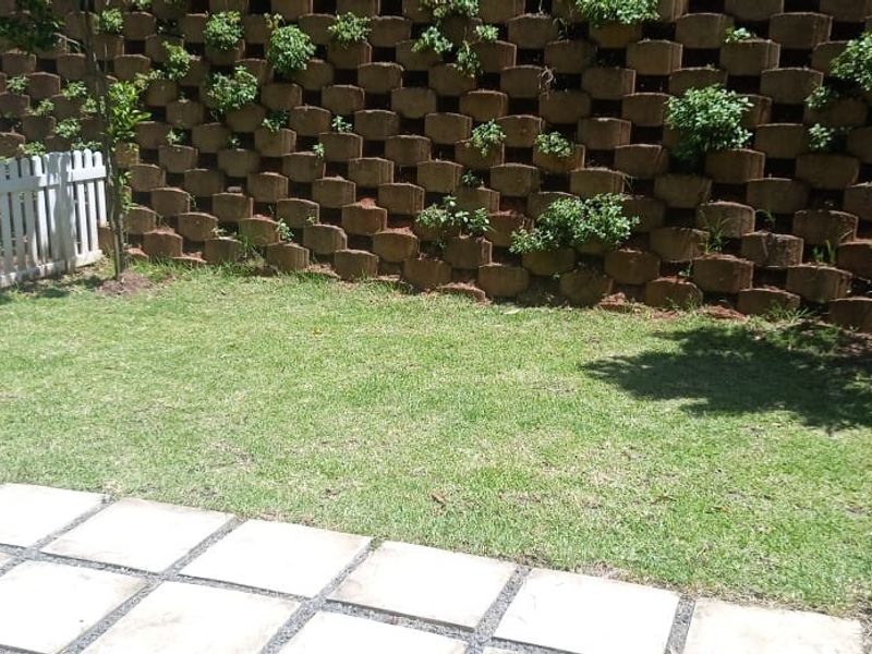 A private garden area featuring a manicured lawn, paved patio section, white picket fencing, and a tiered stone retaining wall with integrated greenery.