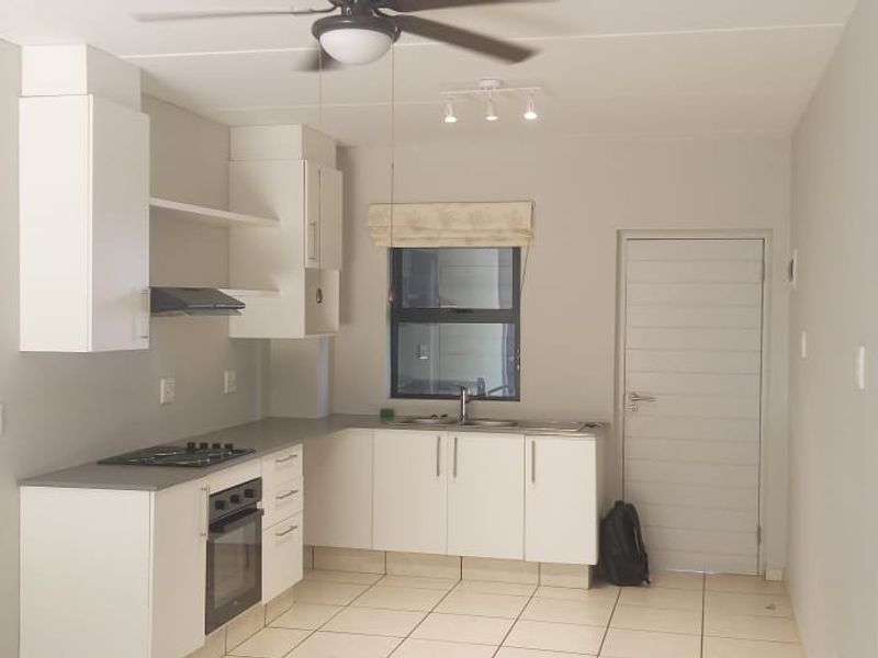 A clean, functional kitchen featuring white cabinetry, dark countertops, built-in oven, gas hob, and tiled flooring in an open-plan layout.