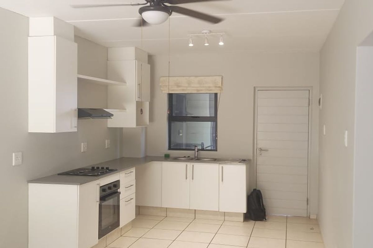 A clean, functional kitchen featuring white cabinetry, dark countertops, built-in oven, gas hob, and tiled flooring in an open-plan layout.