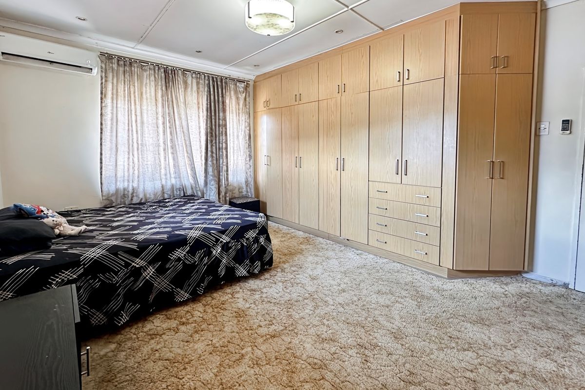 Spacious bedroom featuring extensive built-in wooden cabinetry, wall-mounted air conditioning unit, and neutral carpeting.