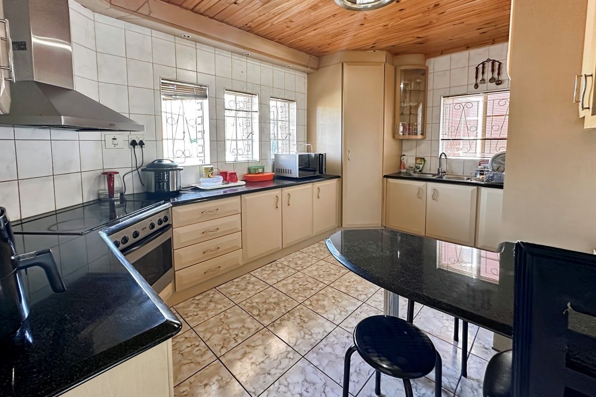 A functional kitchen featuring dark granite countertops, built-in cabinetry, a stainless steel extractor fan, and a timber-clad ceiling.