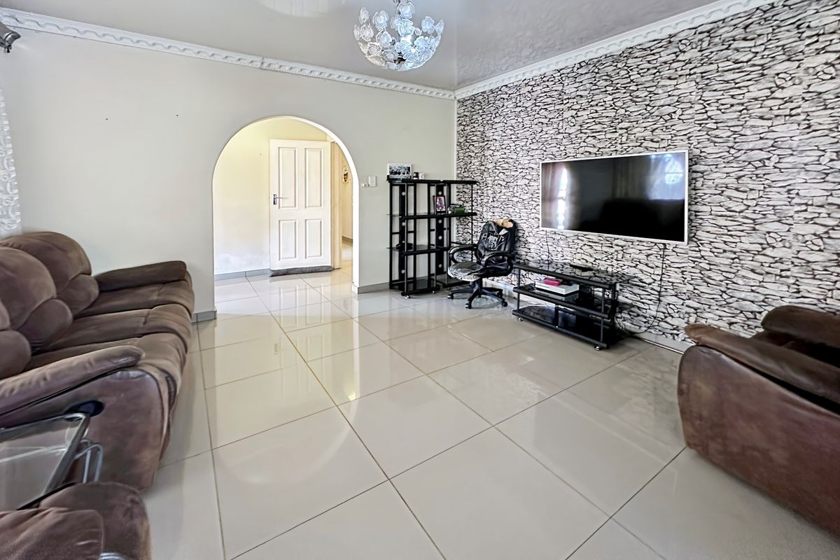 Spacious living room featuring polished porcelain floor tiles, decorative crown molding, and a textured stone-effect feature wall.