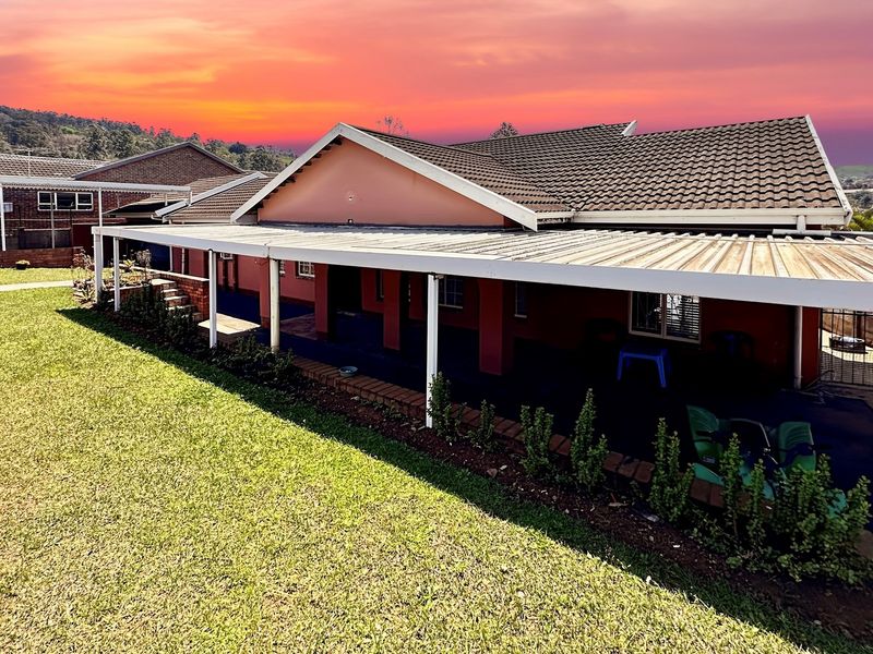 Rear view of the house featuring a large covered patio area, tiled roof, and established lawn under a sunset sky.
