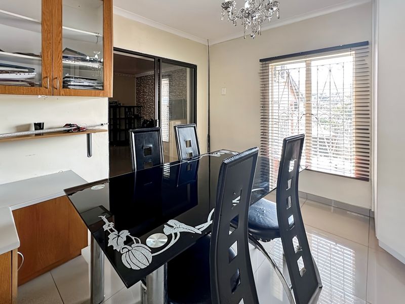 A dining area featuring tiled flooring, built-in wooden cabinetry, and a window with security bars, providing a functional space for meals.