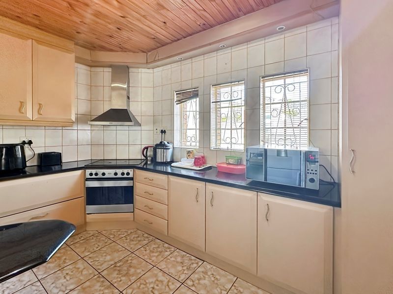A functional kitchen featuring light-toned cabinetry, dark countertops, a built-in oven with extractor fan, and tiled flooring under a timber-paneled ceiling.