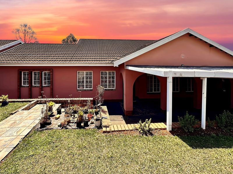 A single-story residential home featuring a tiled roof, covered patio area, and a paved walkway set against a sunset backdrop.