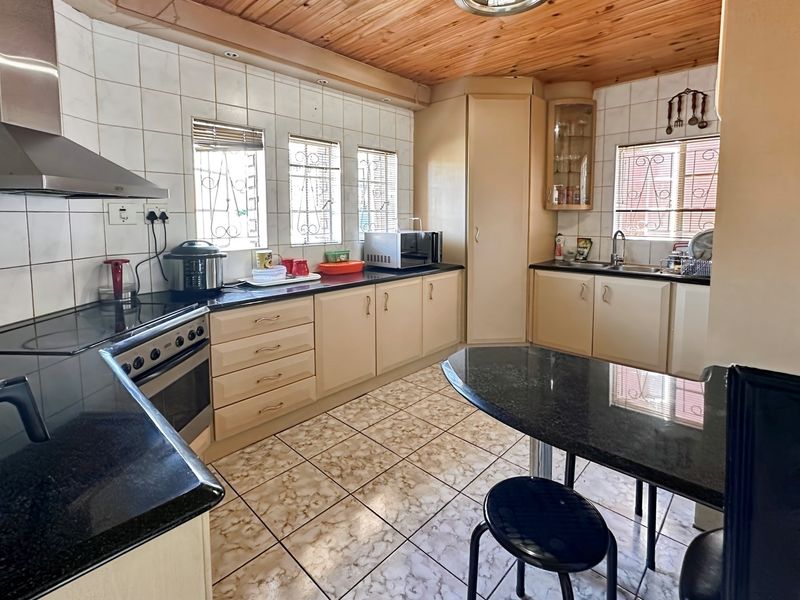 A functional kitchen featuring dark granite countertops, built-in cabinetry, a stainless steel extractor fan, and a timber-clad ceiling.