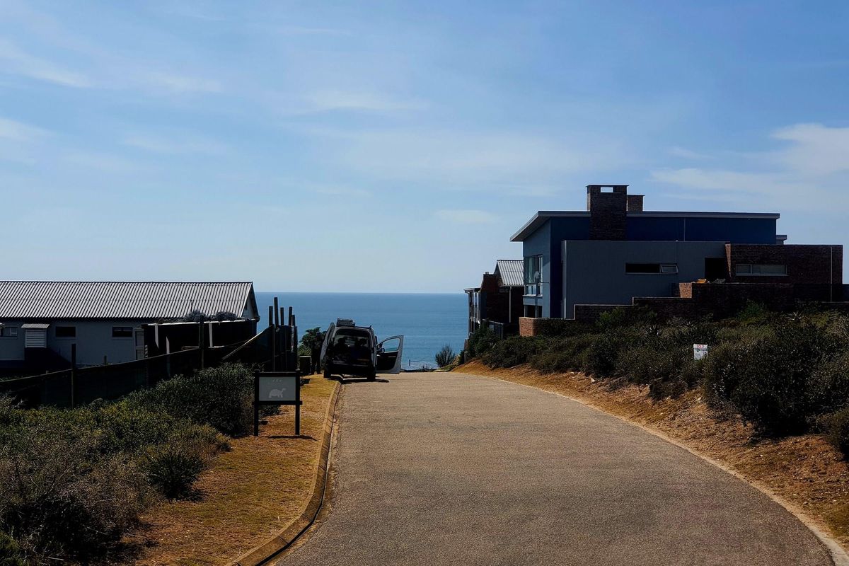 A view of a paved residential street leading towards the ocean, showcasing the coastal setting and surrounding neighborhood architecture.