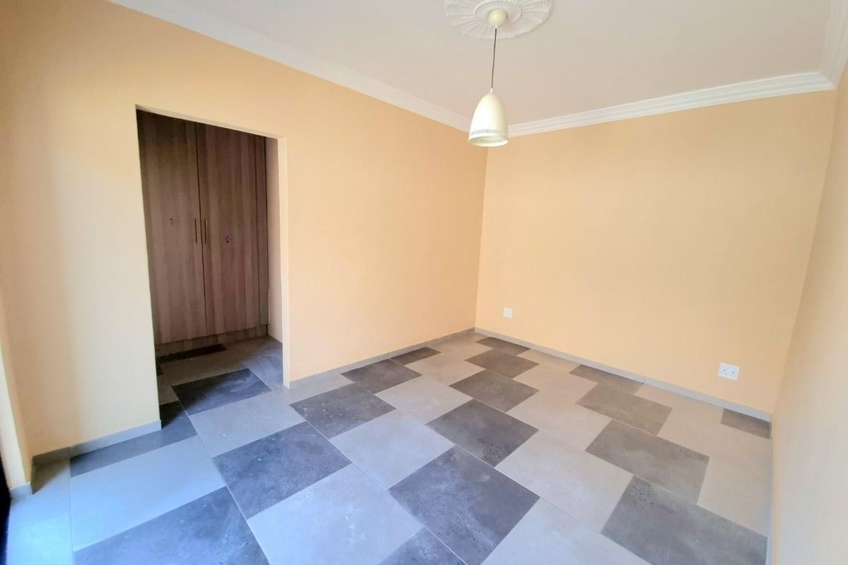 A clean, empty bedroom featuring modern checkered floor tiles, built-in cupboards, and a decorative ceiling rose with a pendant light fixture.