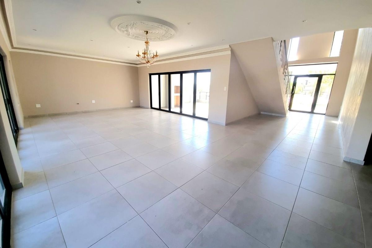 Spacious, open-plan living area featuring large format floor tiles, a decorative ceiling rose with chandelier, and expansive sliding glass doors leading to the exterior.
