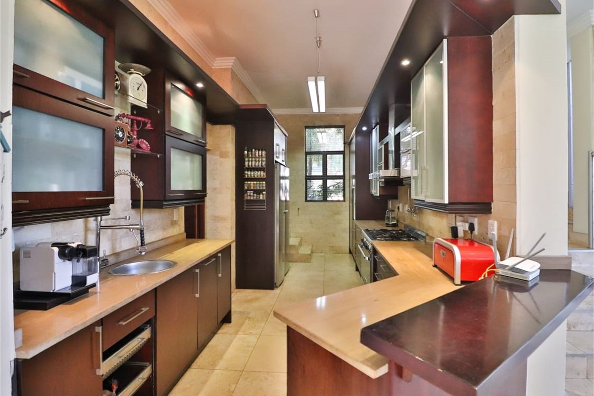 A well-appointed galley-style kitchen featuring dark wood cabinetry, stone countertops, integrated gas hob, and tiled flooring with ample storage space.