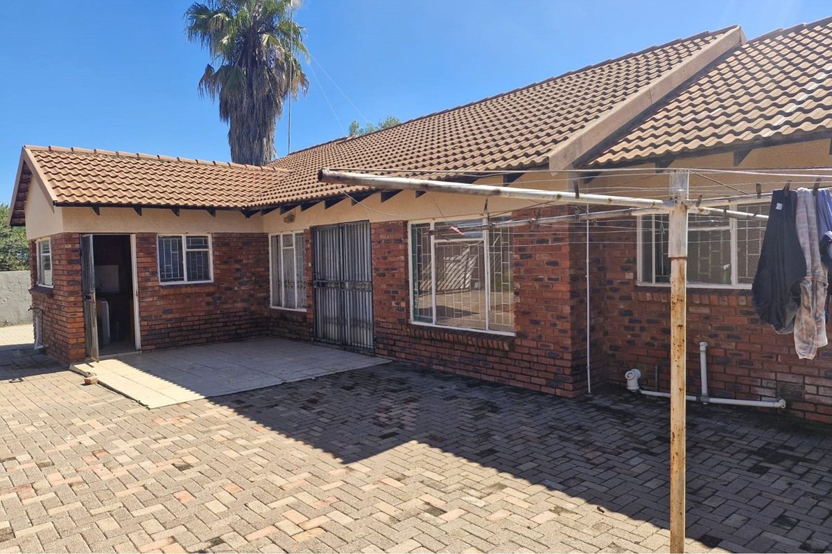 Rear view of a face brick house featuring a paved courtyard, tiled roof, and secure window and door access points.