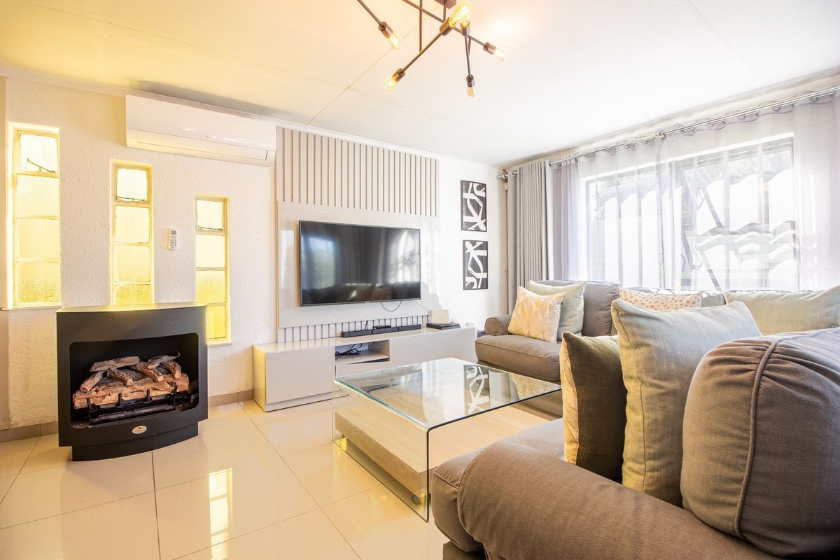 A well-maintained living room featuring a modern fireplace, split-system air conditioning, tiled flooring, and contemporary wall paneling.
