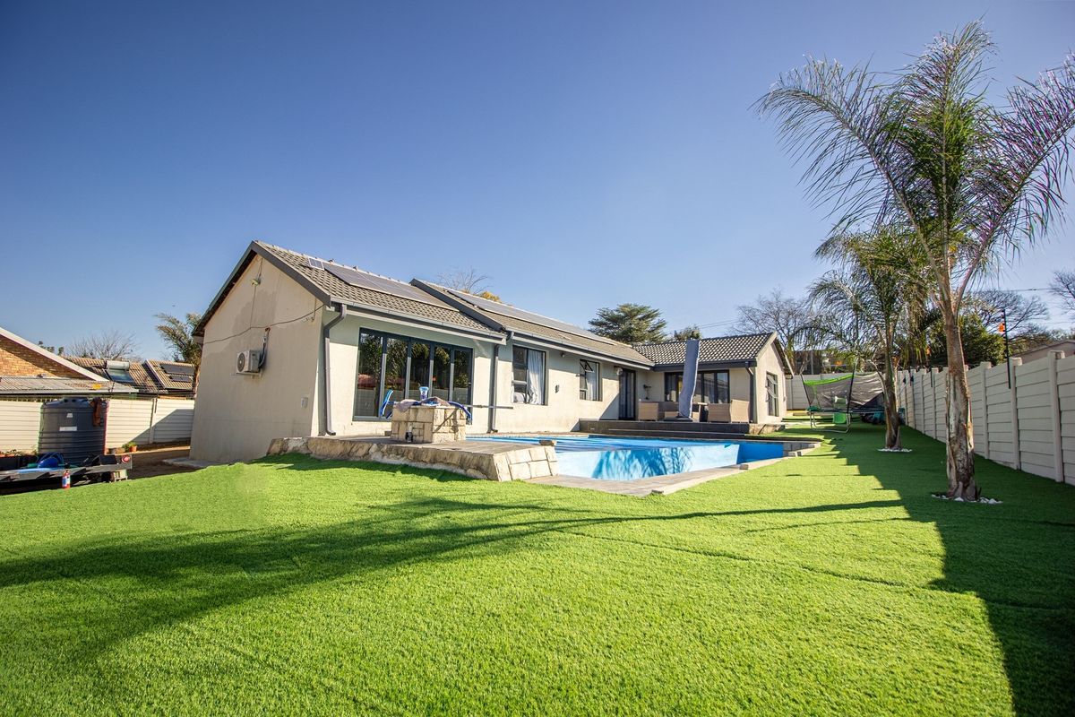 Rear view of the property featuring a swimming pool, artificial lawn, solar panels on the roof, and sliding glass doors leading to the interior.