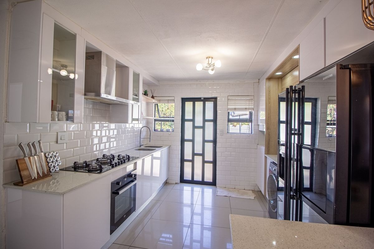 Modern, well-appointed kitchen featuring sleek white gloss cabinetry, stone countertops, subway tile backsplash, and integrated gas hob and oven.