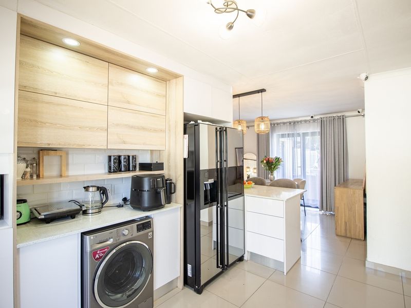 Modern open-plan kitchen featuring light wood-tone cabinetry, stone countertops, subway tile backsplash, and integrated laundry facilities, flowing into a bright dining area.