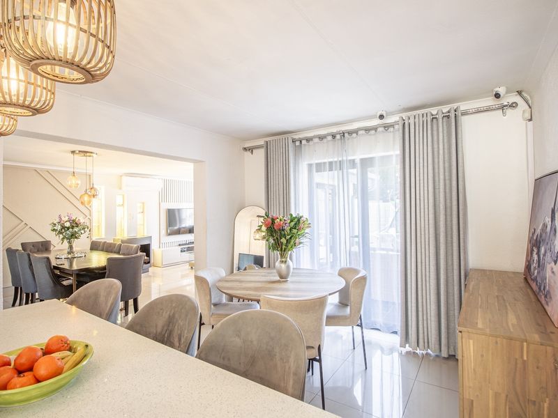 Bright open-plan living and dining area featuring tiled floors, modern lighting, and large sliding glass doors providing access to the outdoor space.