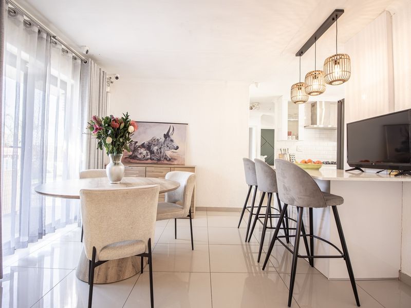 A bright open-plan living and dining area featuring a modern kitchen island with pendant lighting and sleek tiled flooring throughout.